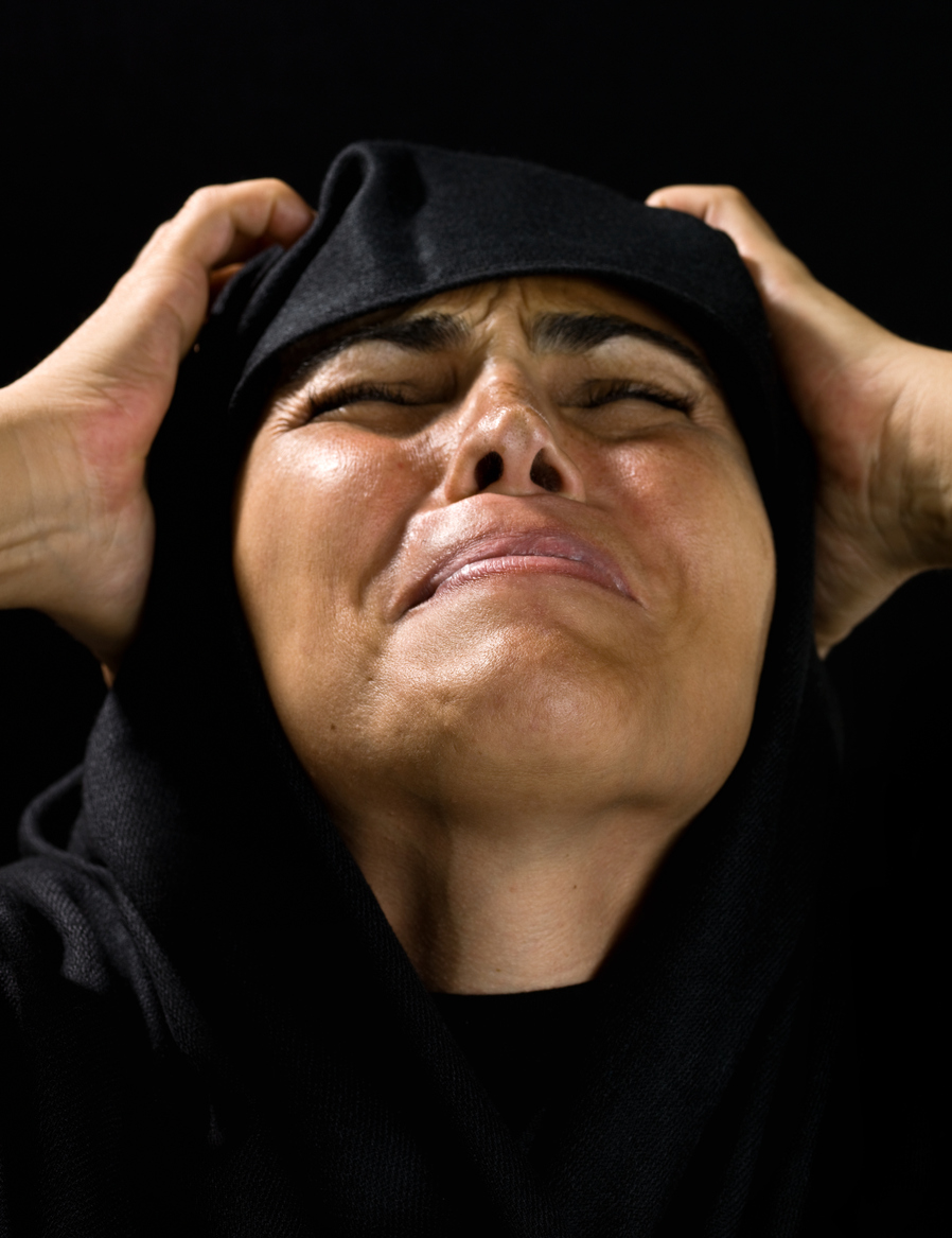 A woman in a black headscarf throws her head back in anguish